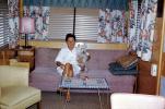 Woman sits on a Sofa, couch, lamp, coffee table, mod, Dog, lampshade, Trailer Home, curtains, 1960s, PDFV02P05_01